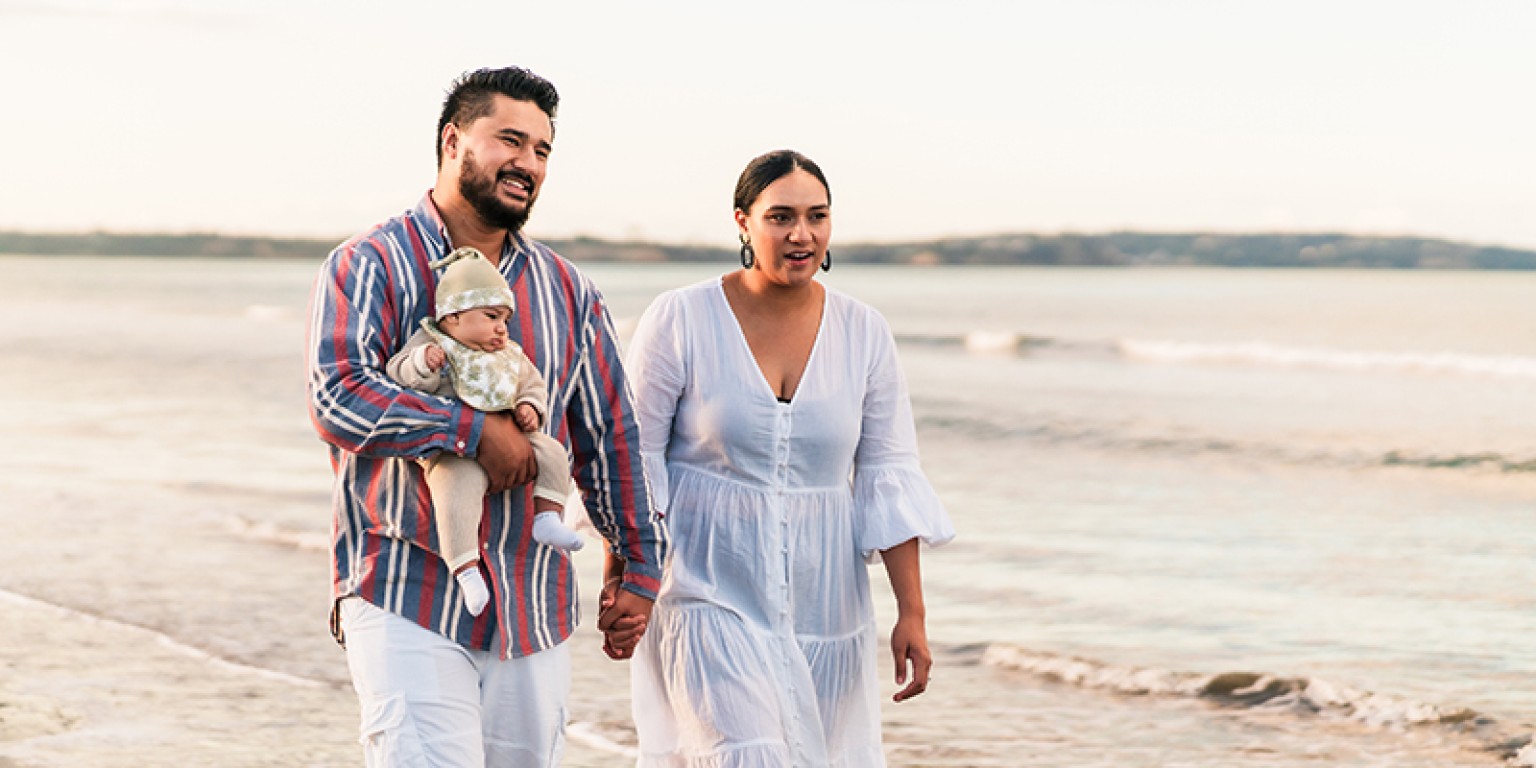 photo of couple walking down a beach with a baby